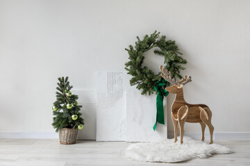 Christmas wreath, tree and wooden deer near light wall in room