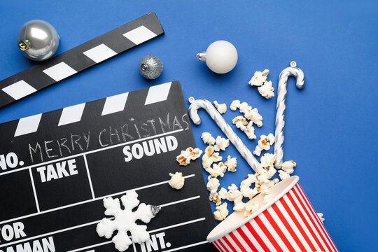Movie clapper, bucket of popcorn and Christmas balls on blue background