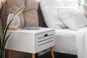 Bedside table with lamp and magazine in light bedroom, closeup