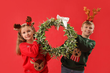 Little children in reindeer horns with Christmas mistletoe wreath on red background
