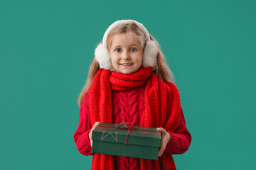 Little girl in earmuffs with Christmas gift on green background
