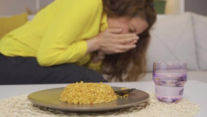 A woman who is sick to her stomach as a result of food poisoning.
The woman holding her stomach gets poisoned from the food she eats and vomits.
