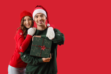Young couple in love with Christmas gift on red background