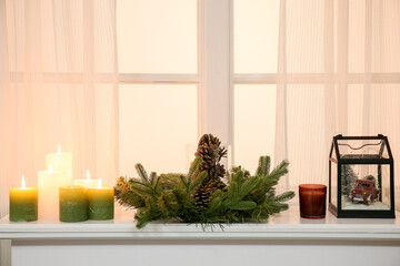 Christmas wreath with burning candles on mantelpiece near window