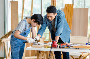 Asian professional carpenter engineer dad teaching young boy son in jeans outfit with gloves safety...