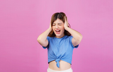 Obraz na płótnie Canvas Portrait of angry irritated young woman wearing casual t-shirt covering her ears with hands and shouting while standing isolated over pink background