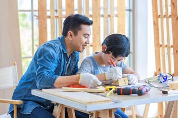 Asian professional male carpenter woodworker engineer dad in jeans outfit with safety gloves holding small home model teaching young boy son using measuring square ruler in housing construction site