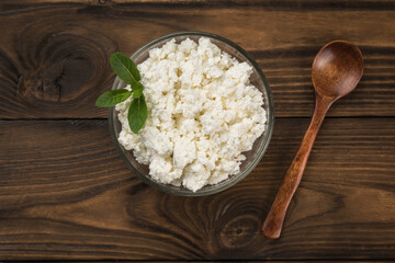 A wooden spoon and a glass plate with cottage cheese on a wooden table.