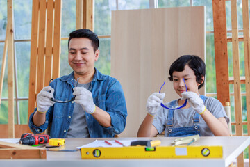 Asian professional carpenter engineer architect woodworker dad and amateur young boy sitting wearing safety goggles and gloves together preparing to work in housing home building construction site