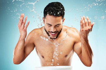 Studio, water splash and face skincare of man isolated against a blue background. Health, hygiene...