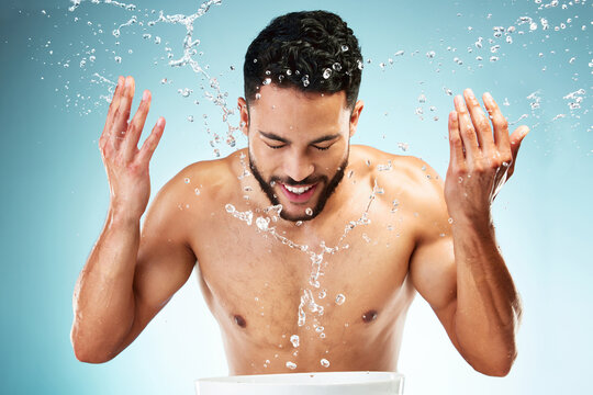 Studio, water splash and face skincare of man isolated against a blue background. Health, hygiene and male model washing face, cleaning and grooming routine for wellness, beauty or facial freshness.