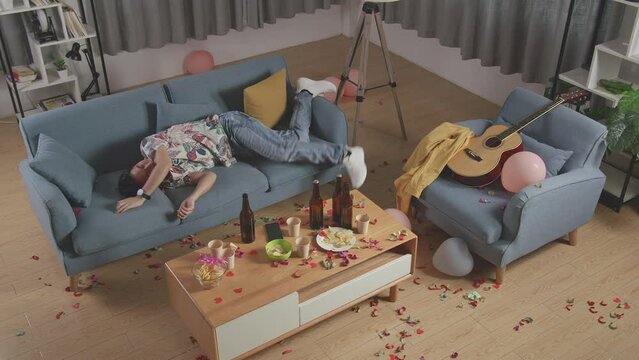 Top View Of Drunk Asian Man Wakes Up After Sleeping On A Sofa Then Looking Around In The Party Room At Home
