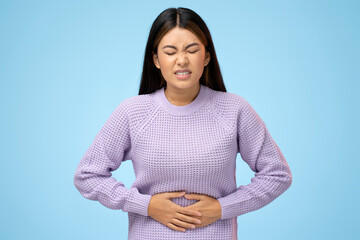 Portrait of beautiful brunette asian young woman standing and feeling pain on her stomach