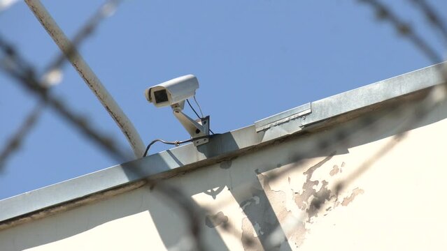 Security camera behind barbed wire fence stretched around prison walls