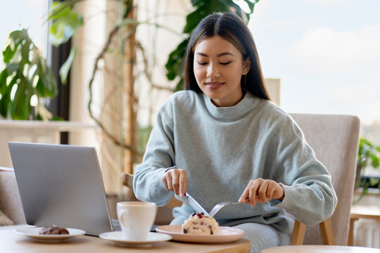 Cute asian girl eating tasty dessert while working at the cozy cafe