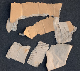 Pieces of brown cardboard paper with torn edges on textured black background