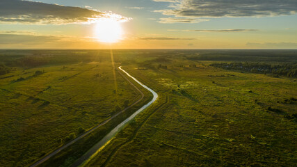 Top view of the countryside, river through fields and sun at sunset