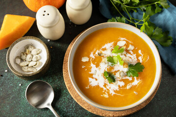 Vegetarian pumpkin and carrot cream soup with cream and pumpkin seeds on a stone tabletop. Comfort...