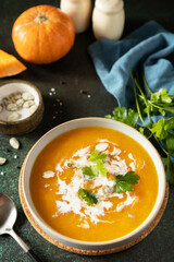 Vegetarian pumpkin and carrot cream soup with cream and pumpkin seeds on a stone tabletop. Comfort food, fall and winter healthy slow food concept.