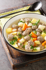 Traditional Norwegian soup Sodd with root vegetables and beef meatballs close-up in a plate on the table. Vertical