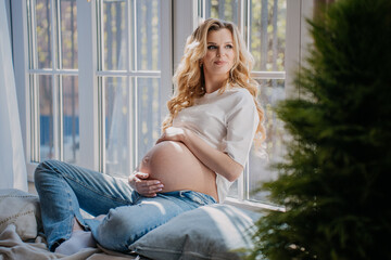 Gorgeous pregnant swedish woman with wavy hair in t-shirt and blue jeans sits on the floor with...