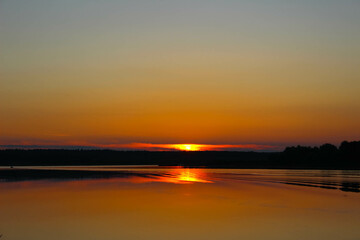 Sunset in strong colors over a river with reflections of trees