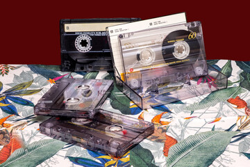 Vintage cassette tapes on a floral table with a maroon background.