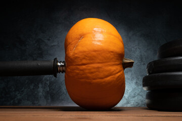 Dumbbell barbell with orange pumpkin as a weight plate. Gym weightlifting workout and sport...