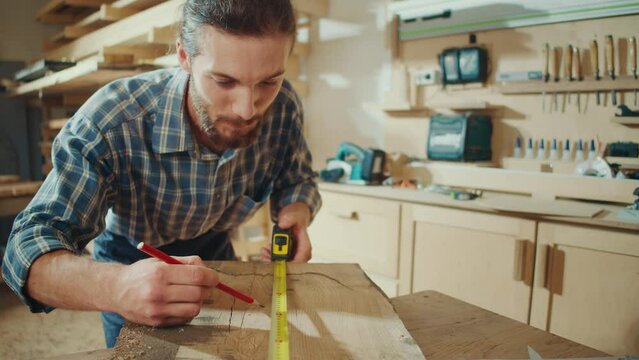 Attractive Carpenter Using a Tape Measure Ruler to Measuring Wood Board in a Loft Studio with Tools on the Walls. Woodworking. Manual Labor. Factory. Carpentry, Craftsmanship, and Handwork Concept.
