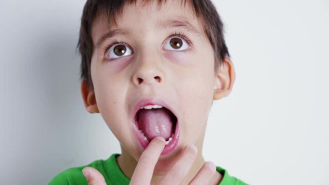 boy child in a green T-shirt shows his mouth without front baby teeth and shows a tooth to the camera , standing on a white background to the room