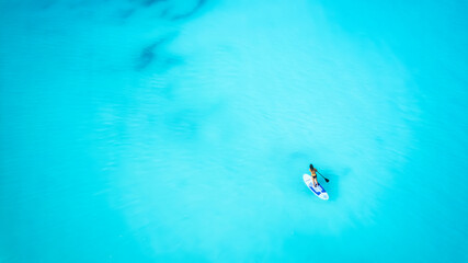 Aerial top down view of a woman on a stand up paddle (SUP) board over the turquoise Caribbean ocean...