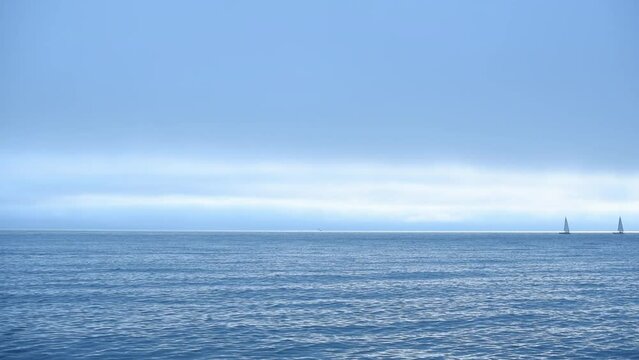 Slow motion of beautiful blue sea with two yachts on the horizon against blue sky. Beauty of nature concept
