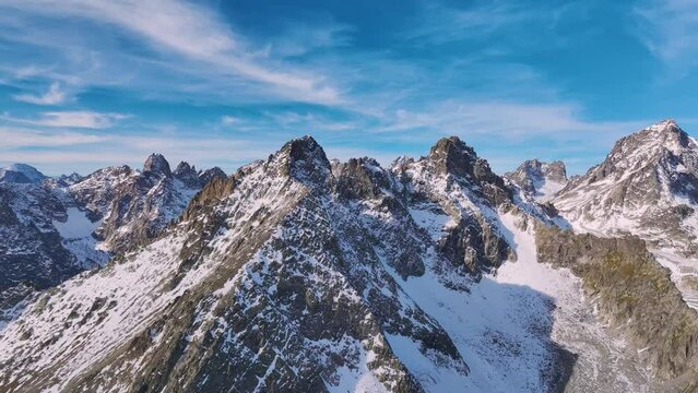 Close flight approach to the snow-capped peaks of the rocky mountain ranges high in the mountains. Mountain peaks on a sunny day lifeless landscape aerial view
