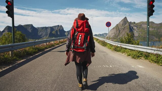 happy girl traveler with a backpack on the road in Norway lofoten, traveling to northern Europe, adventure hiking hitchhiking