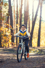 Fototapeta na wymiar Happy kid boy having fun in autumn forest with a bicycle on beautiful fall day.