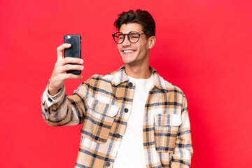 Young caucasian handsome man isolated on red background making a selfie