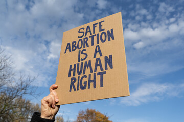 Woman hand holding sign with slogan Safe abortion is a human right. Female protester with placard...
