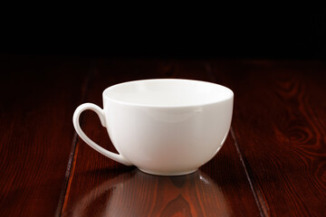 A white, clean, busty china cup against a dark wooden table. Side view.