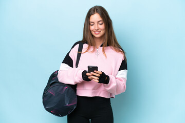 Young sport woman with sport bag isolated on blue background sending a message with the mobile