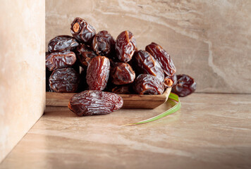Dates fruit in a wooden dish on a beige ceramic table.
