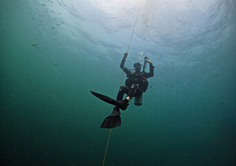Scuba diver in tropical waters hanging on to diving rope - under angled shot with the scuba diver in the middle of the frame - in southern Thailand