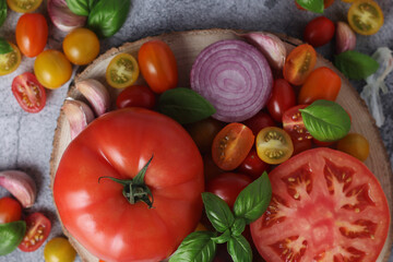 Flat lay composition of different tomatoes, onion, basil and garlic	