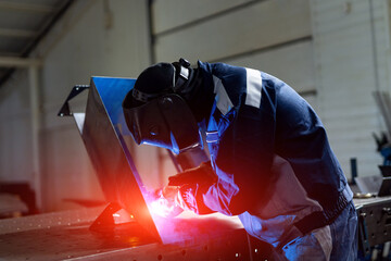 Handsome worker in uniform with metalwork. Man welding metal in protective hat.