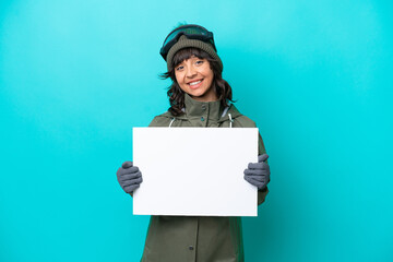 Skier latin woman with snowboarding glasses isolated on blue background holding an empty placard...