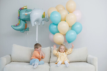 Obraz na płótnie Canvas Girl and boy with color balloons on the sofa