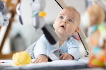 Cute baby boy playing with hanging toys arch on mat at home Baby activity and play center for early...
