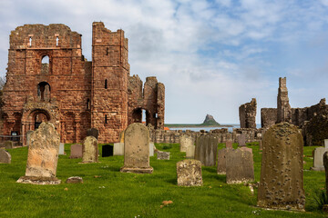 Fototapeta na wymiar The ruins of Lindisfarne Priory and in the distance, Lindisfarne Castle, from the graveyard of the church of St. Mary the Virgin, Holy Island, Northumberland, England