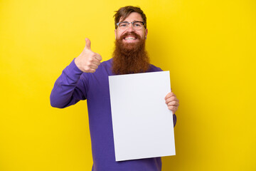 Redhead man with beard isolated on yellow background holding an empty placard with thumb up