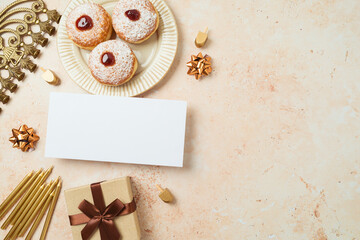 Greeting card mock up for Hanukkah holiday. Traditional donuts, menorah and gift box on stone background. Top view, flat lay