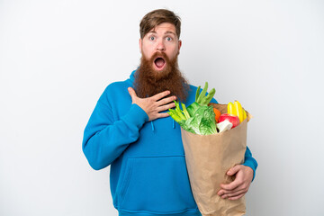 Redhead man with beard holding a grocery shopping bag isolated on white background surprised and shocked while looking right